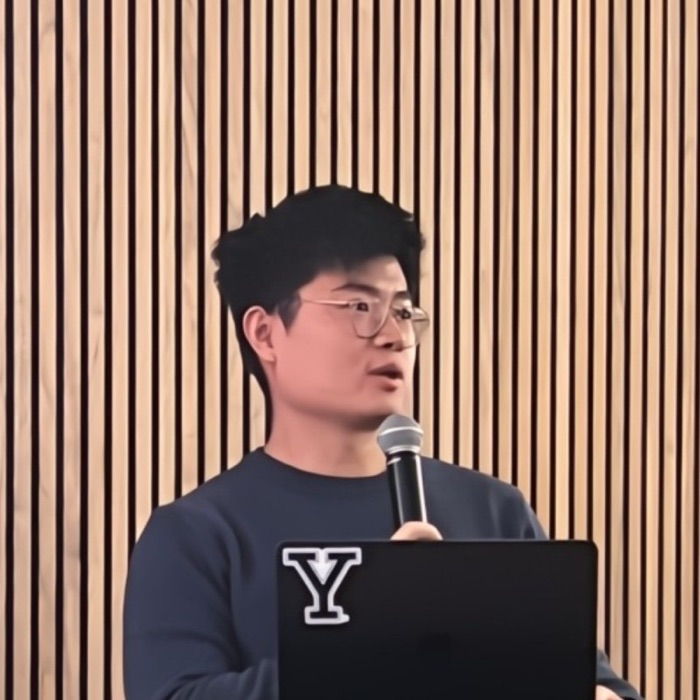 Shaun Zhang giving a talk, mic in hand, behind a laptop with a Yale sticker